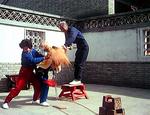 Hou Shuying breaks bricks over his son Yung's back while his wife, Suen, supports him. There is a spear tip at Yung's throat, but because of his Qi Gong training it is unable to penetrate and shatters.